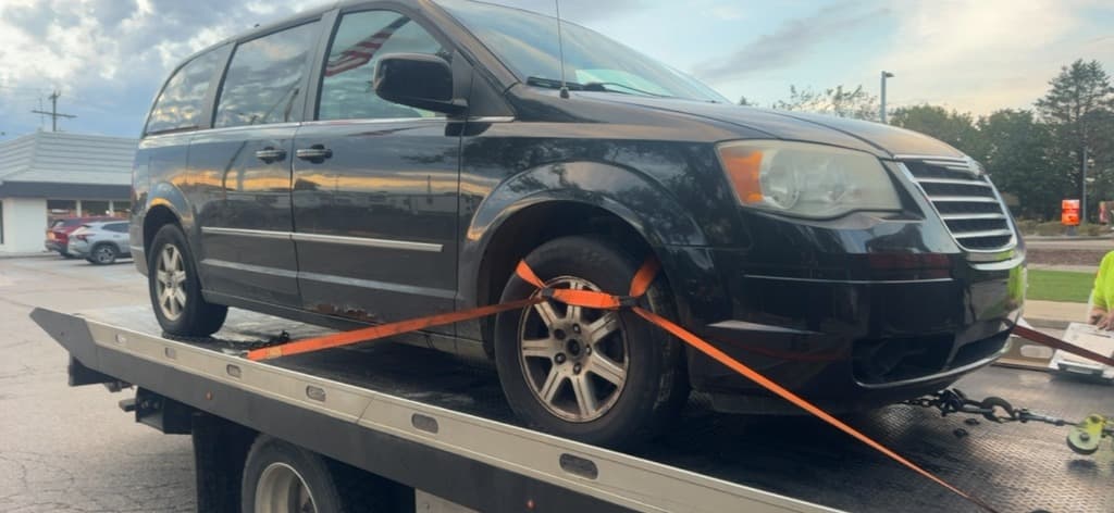 Black Chrysler Town and Country minivan secured with tow straps on a flatbed